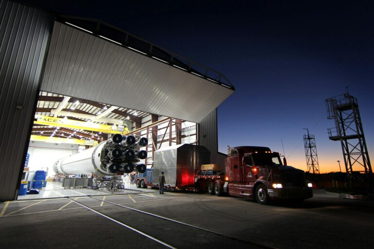 A large rocket being moved from a hangar at twilight, showcasing advanced engineering and space technology.